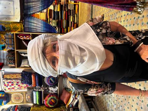 Close-up portrait of a traveller trying on a white desert turban inside a colorful textile shop.