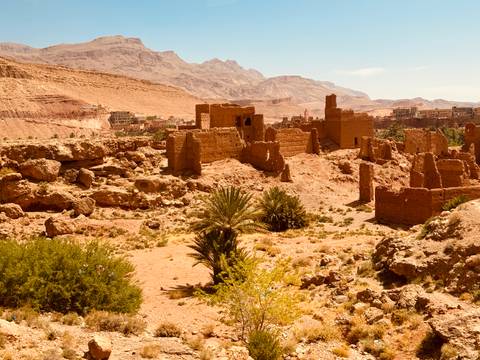 Ruined adobe fortress structures scattered across a rocky desert valley with mountains behind.