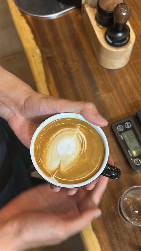 Close-up of a hand holding a cup of cappuccino with clear heart-shaped latte art.