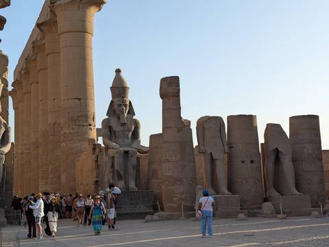 Visitors explore the grand columns and seated pharaoh statues of Luxor Temple under soft evening light.