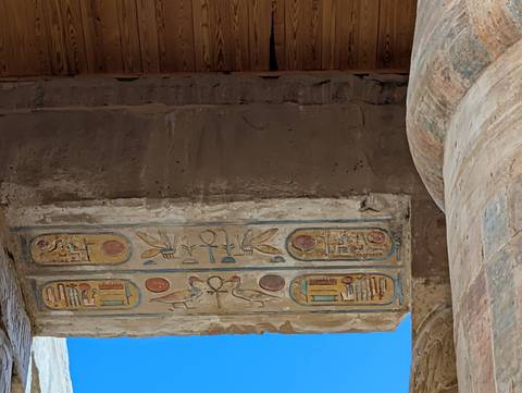 Colorful hieroglyphic carvings decorate the underside of an ancient stone lintel against a bright blue sky.