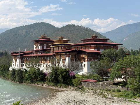 Punakha Dzong’s ornate red-roofed buildings rise above blooming trees beside a glacial river and forested hills.