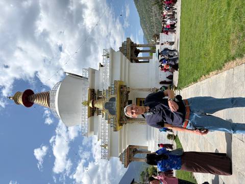 A tourist smiles in front of the white Memorial Chorten stupa while other visitors circulate around it.