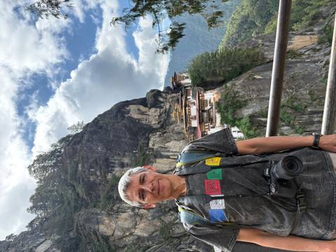 Traveler stands on a railing with Bhutan’s cliff-hanging Tiger’s Nest Monastery visible across the gorge.