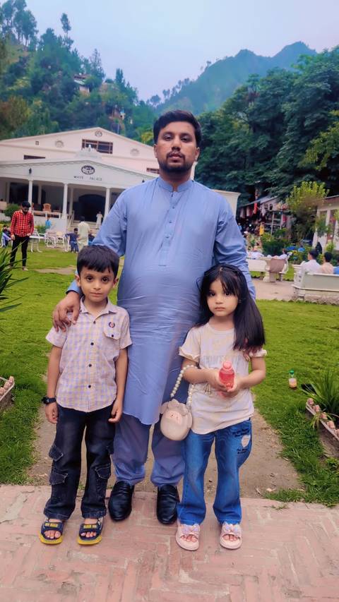 Father poses with two young children on a grassy restaurant lawn bustling with visitors.