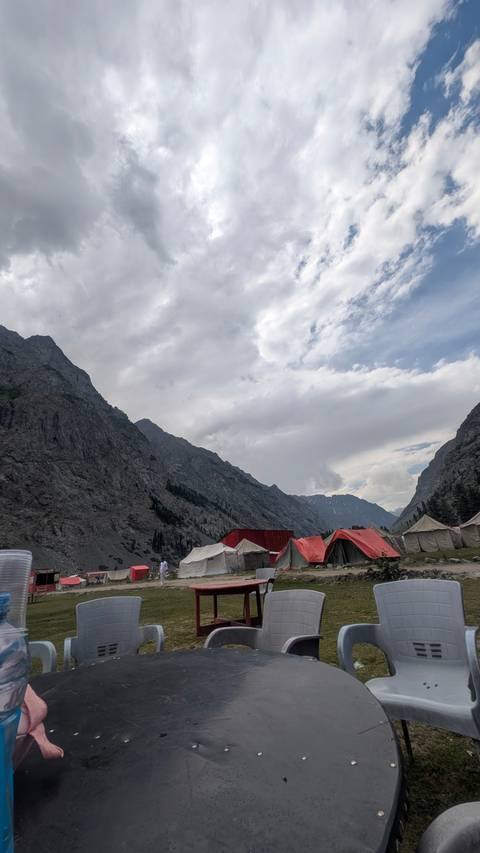 Mountain valley lined with red-roofed tents beneath towering gray cliffs under a dramatic sky.