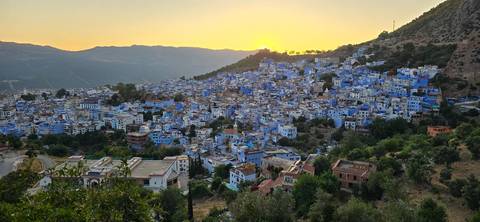 A panoramic sunset view over the blue-painted houses of Chefchaouen nestled in rolling hills.