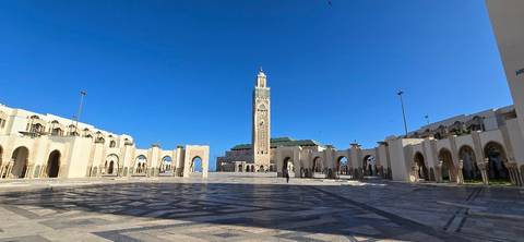 Wide plaza leading to the Hassan II Mosque with its soaring minaret against a cloudless deep-blue sky.