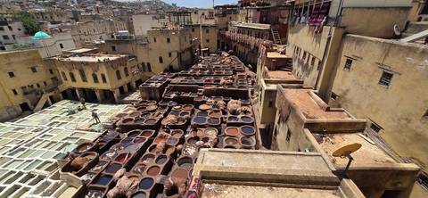 Elevated view of Fes’s ancient tannery filled with multicolored dye vats surrounded by yellowed buildings.
