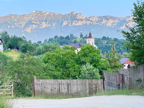 Village church spire rising above lush trees with hazy mountain backdrop and rustic fence in foreground.