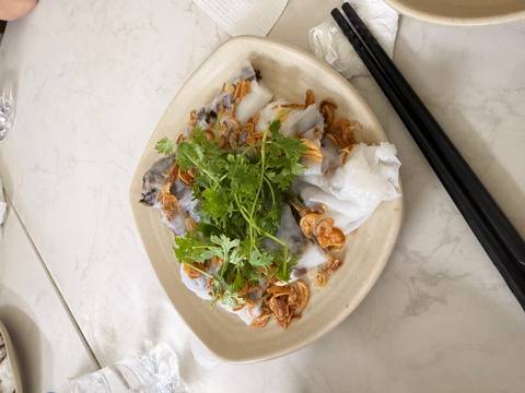 Plate of steamed rice rolls filled with mushroom, topped with fried shallots and fresh cilantro.