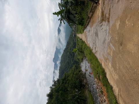 Misty mountains loom beyond a rural path beside a small river in northern Vietnam countryside.