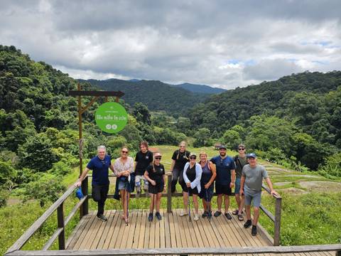 Small tour group posing on a wooden platform overlooking lush green mountains and terraced fields