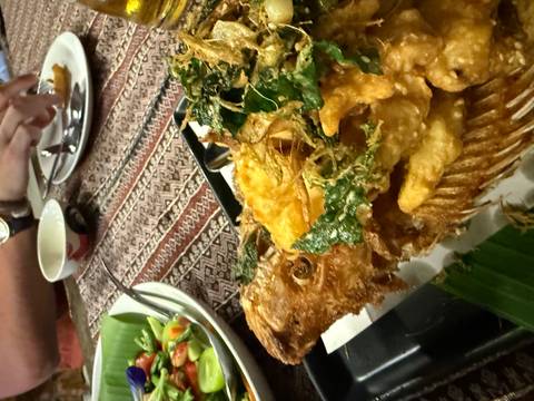 Close-up of deep-fried whole fish topped with crispy herbs on a patterned tablecloth