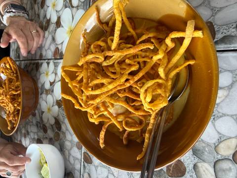 Bowl of creamy curry noodles topped with crispy fried noodles on a floral tiled table