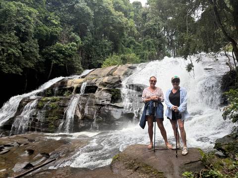Two women posing on rocks in front of a cascading forest waterfall