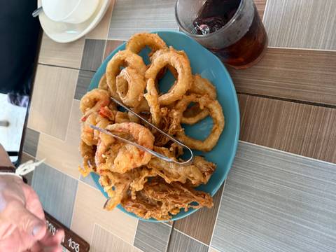 Plate piled with assorted deep-fried onion rings and vegetables on a tiled table