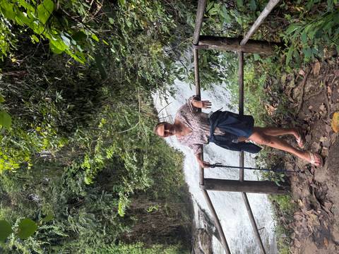 Woman leaning on wooden railing beside rushing waterfall in lush forest