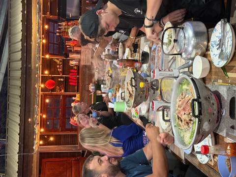 Large group enjoying steaming communal hotpot meal at a rustic outdoor restaurant strung with lights