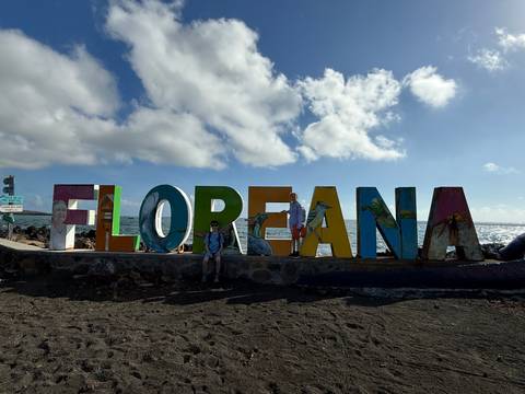 Traveler posing in front of large colorful FLORANA sign on volcanic sand beach with bright sun