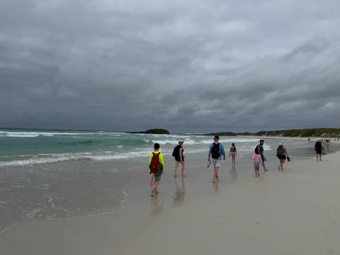 Visitors walking along wide white-sand beach with surf under gray skies