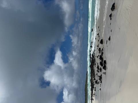 Moody view of empty beach with volcanic rocks, rolling waves and dramatic cloudy sky