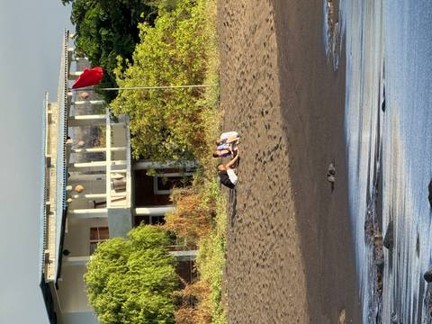 Two people relaxing on dark volcanic sand beach near simple seaside building with red flag