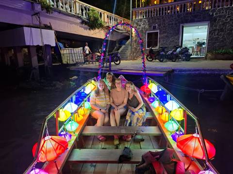 Four women seated in a lantern-lit boat glowing with multicolored lights on a canal at night