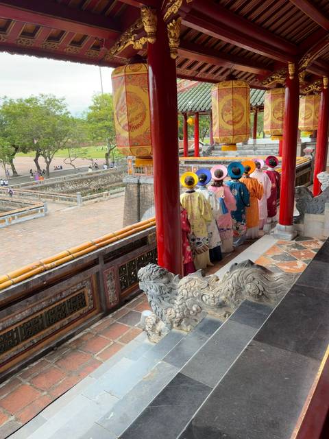 Women in colorful traditional ao dai stand in a row overlooking the imperial courtyard in Hue