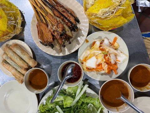 Assortment of Vietnamese street food dishes including spring rolls, grilled skewers and dipping sauces on metal table