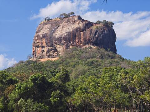 Iconic Sigiriya Rock Fortress rising above tropical forest under a blue sky.