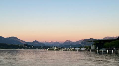 Serene lake scene at dusk with a cruise boat docked against Alpine peaks bathed in pastel sunset hues