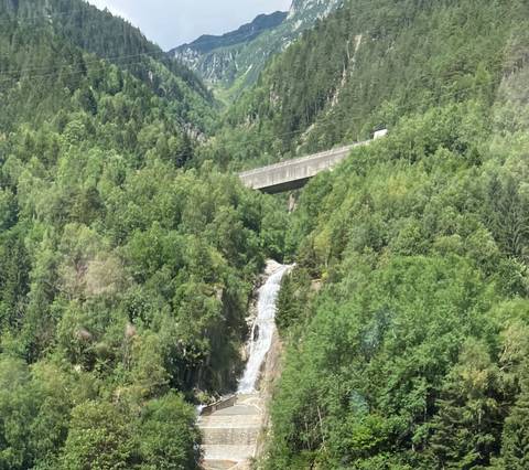 Forest-clad valley with a narrow waterfall dropping beneath a concrete bridge high above the trees