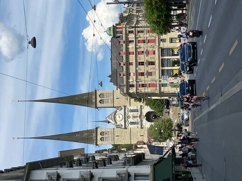 Bustling city street leading to the twin spires of Lucerne’s Church of St. Leodegar under a bright summer sky