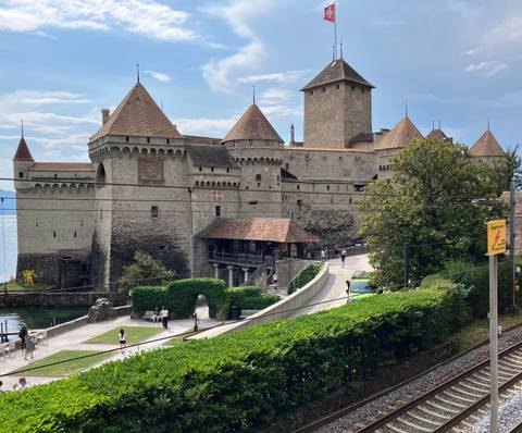Medieval lakeside Château de Chillon with towers and ramparts, visitors walking along the shore road