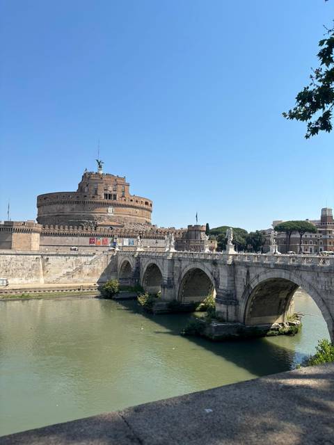 Castel Sant’Angelo and the historic bridge spanning the Tiber River under a bright blue Roman sky