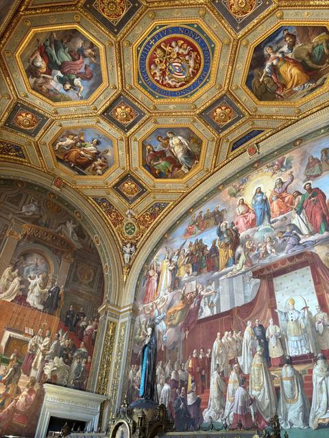 Detailed ceiling and wall frescoes richly framed in gold inside a historic Vatican hall.