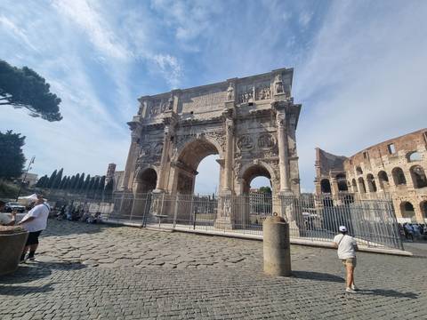 The Arch of Constantine stands majestically beside the Colosseum as visitors gather around.