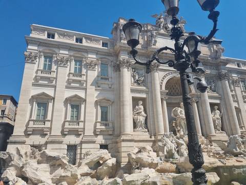 Baroque façade of the Trevi Fountain with marble figures framed by an ornate lamppost.