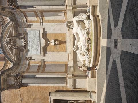 Traveler poses beside a reclining marble river god statue in a Roman courtyard fountain.