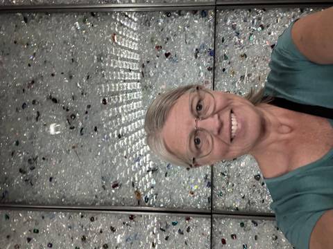 Smiling woman taking a selfie in front of a sparkling crystal-covered wall indoors.