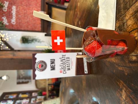 Cup of fresh strawberries dipped in melted chocolate with a small Swiss flag on top, set on a wooden café table.