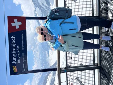 Mother and daughter hug in front of the Jungfraujoch ‘Top of Europe’ sign with snowy alpine peaks behind.