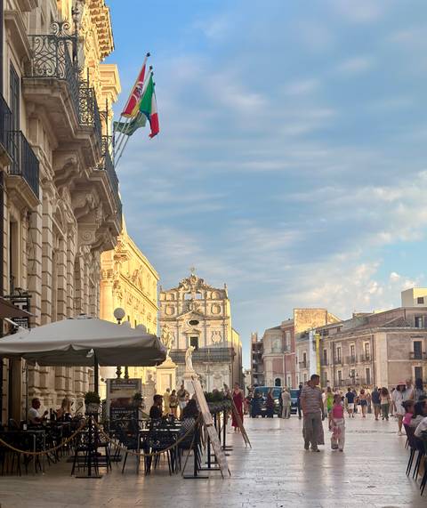 Elegant baroque buildings and a church façade glow under soft evening light in a Sicilian street.