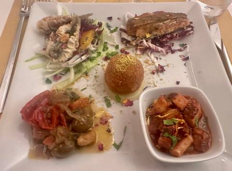 Close-up of an assorted Sicilian antipasto plate with colorful vegetables, croquette and seafood.