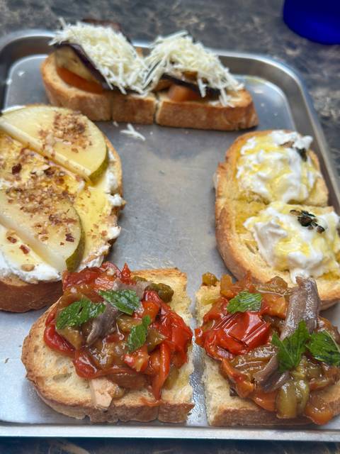 Assorted bruschetta toppings on toasted bread including pear, ricotta and roasted peppers.