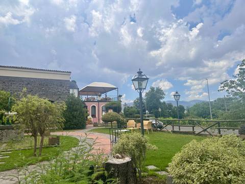 Charming country garden with lawn, lampposts and a stone house under a partly cloudy sky.