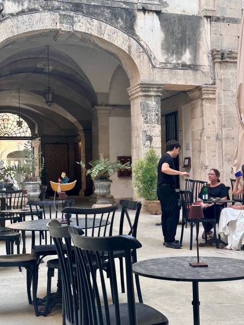 Outdoor café in a historic stone courtyard where a waiter chats with seated guests.