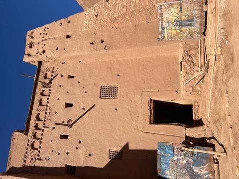 Tall earthen kasbah wall with small windows and decorative crenellations against a deep blue sky.