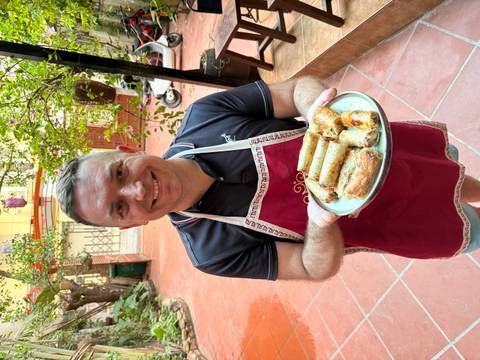 Tourist proudly presents a plate of freshly fried Vietnamese spring rolls while wearing a red apron.